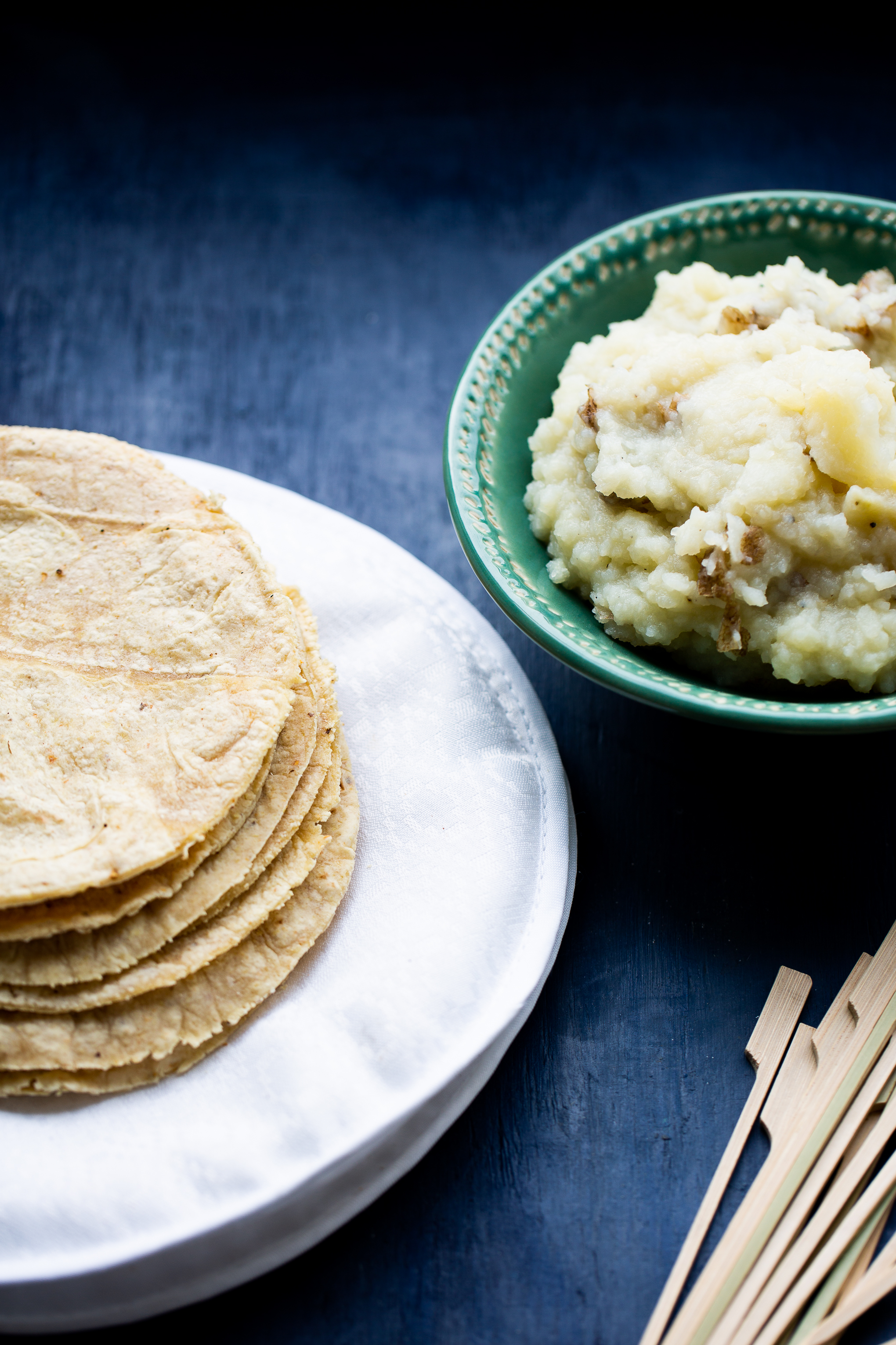 corn tortillas over a withe kitchen towels and a bowl with mashed potatoes.