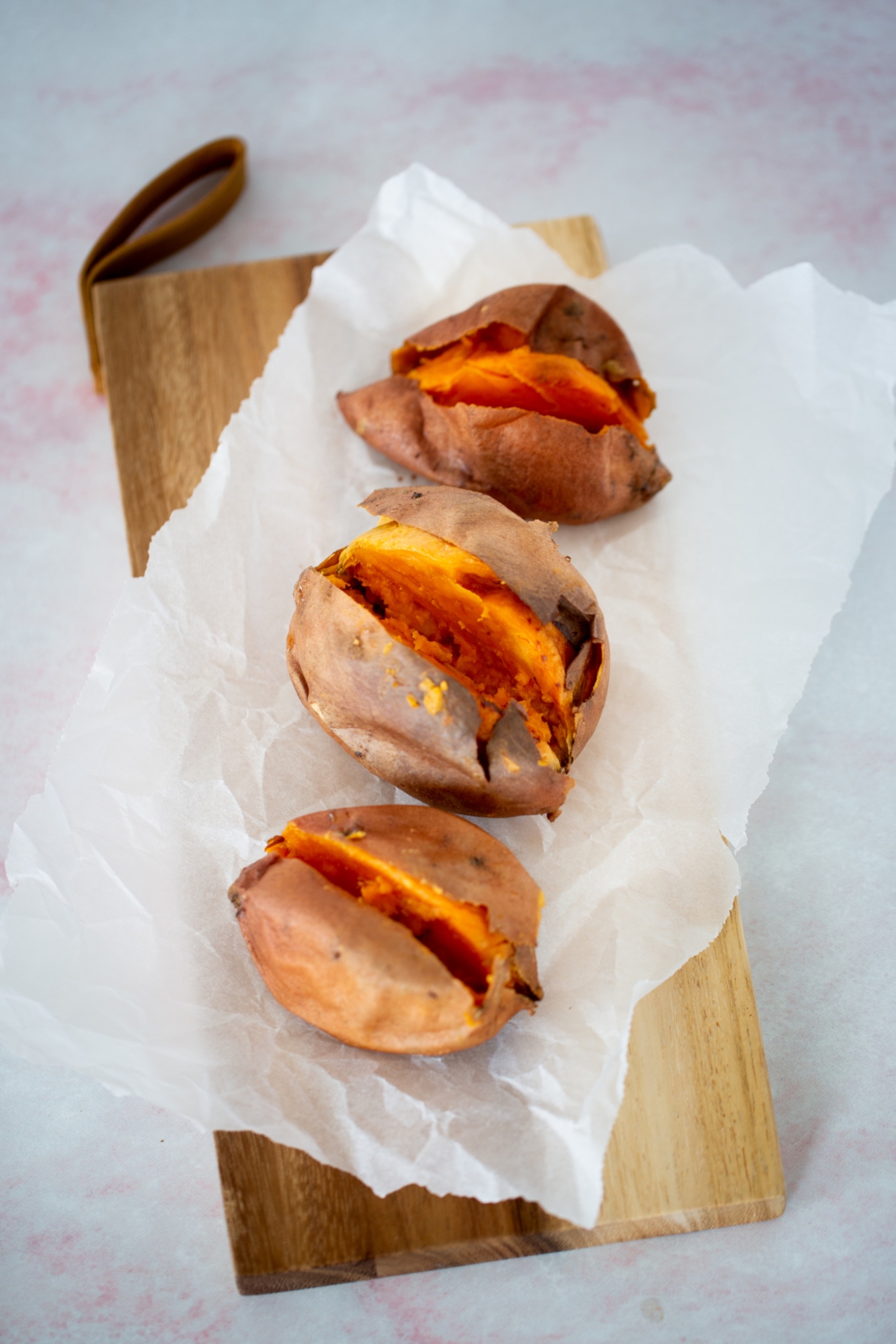 Three cooked sweet potatoes over a cutting board