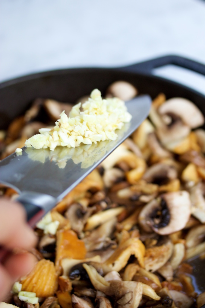 Adding minced garlic to a pan with mushrooms