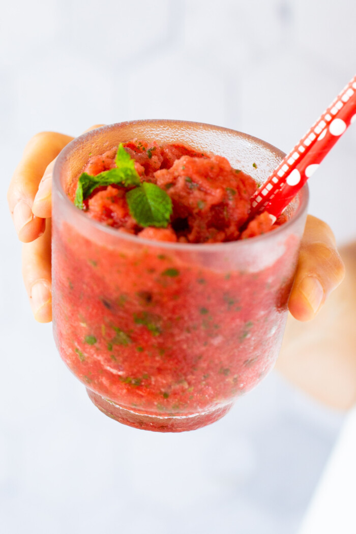 raspado de sandia, watermelon slushie in a clear cup with mint leaves and red straws