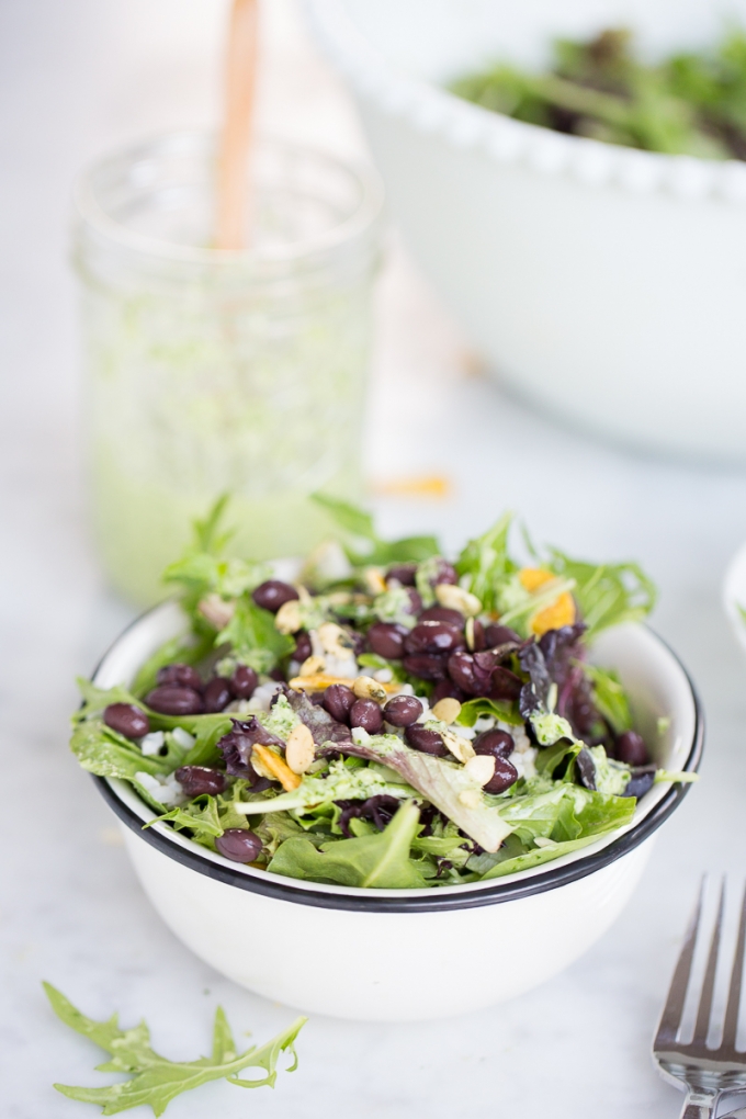 Bowl of salad with black beans, greans and rice with green vegan dressing