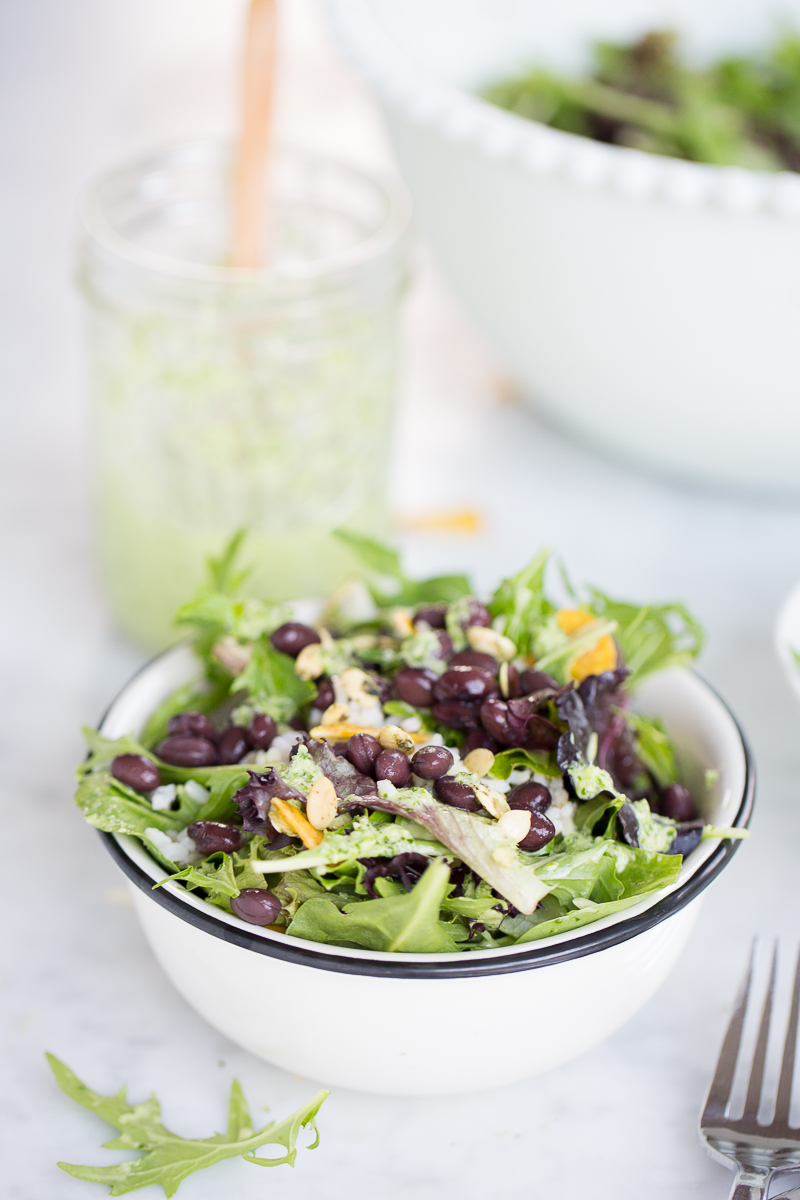 Bowl of salad with black beans, greans and rice with green vegan dressing
