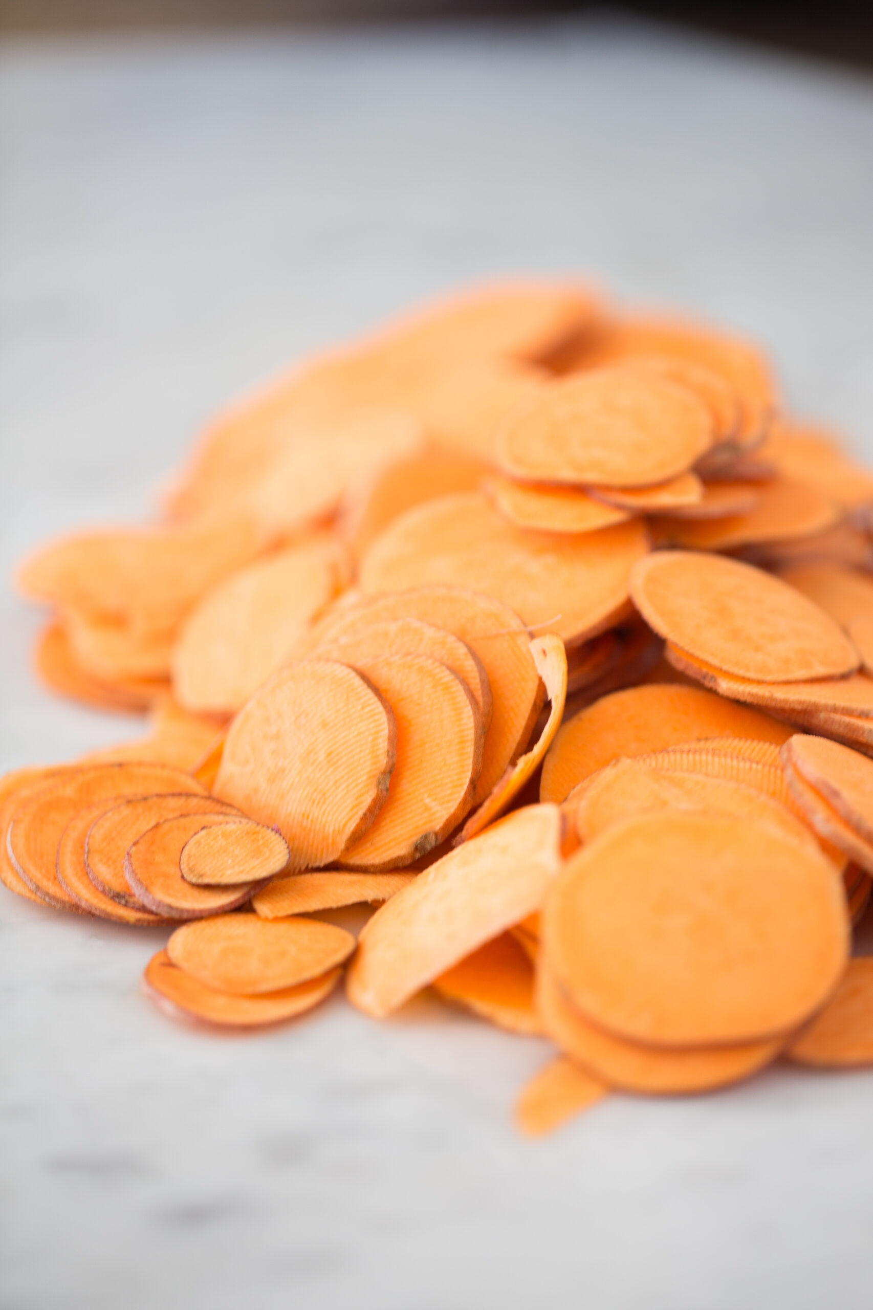 Thinly sliced sweet potatoes on hte white counter top.