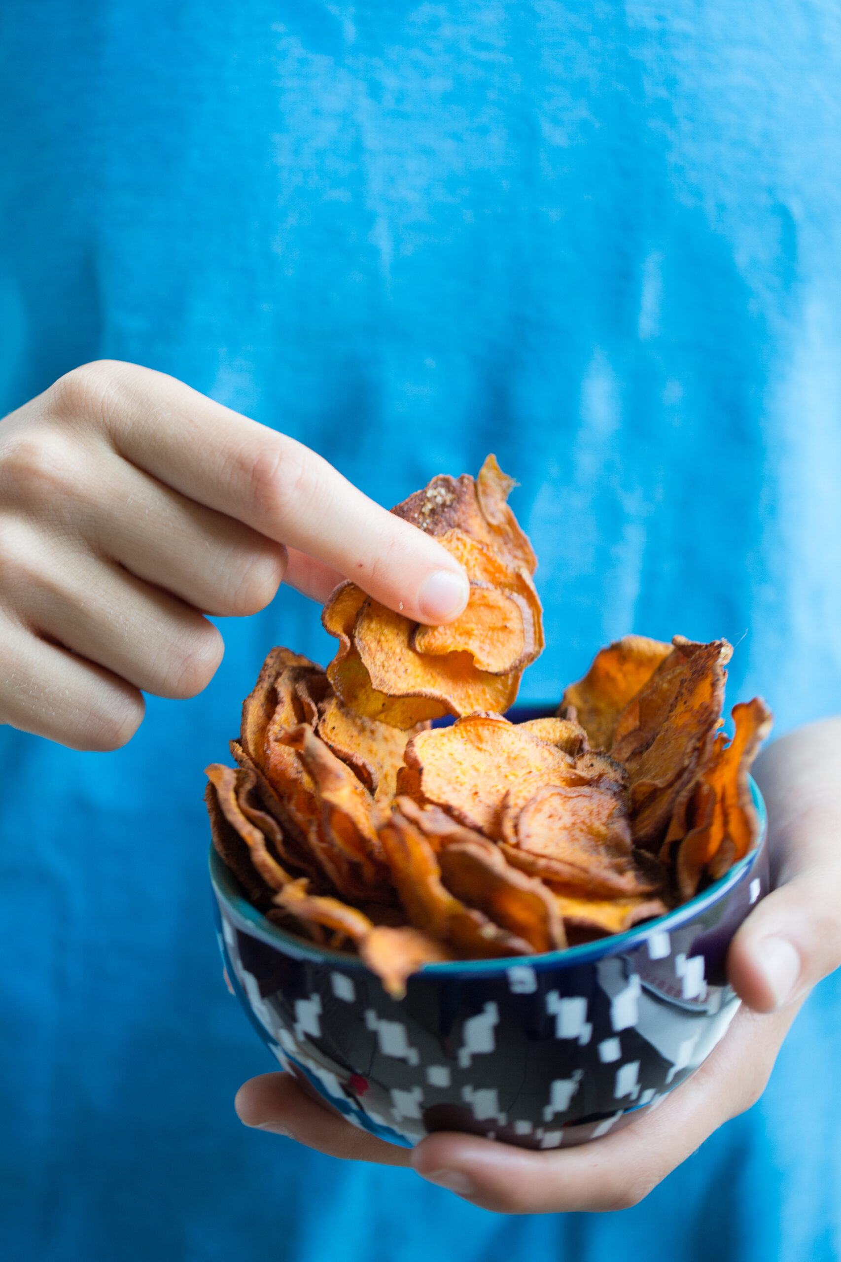 My kid grabbing healthy sweet potato chips from a blue bowl.