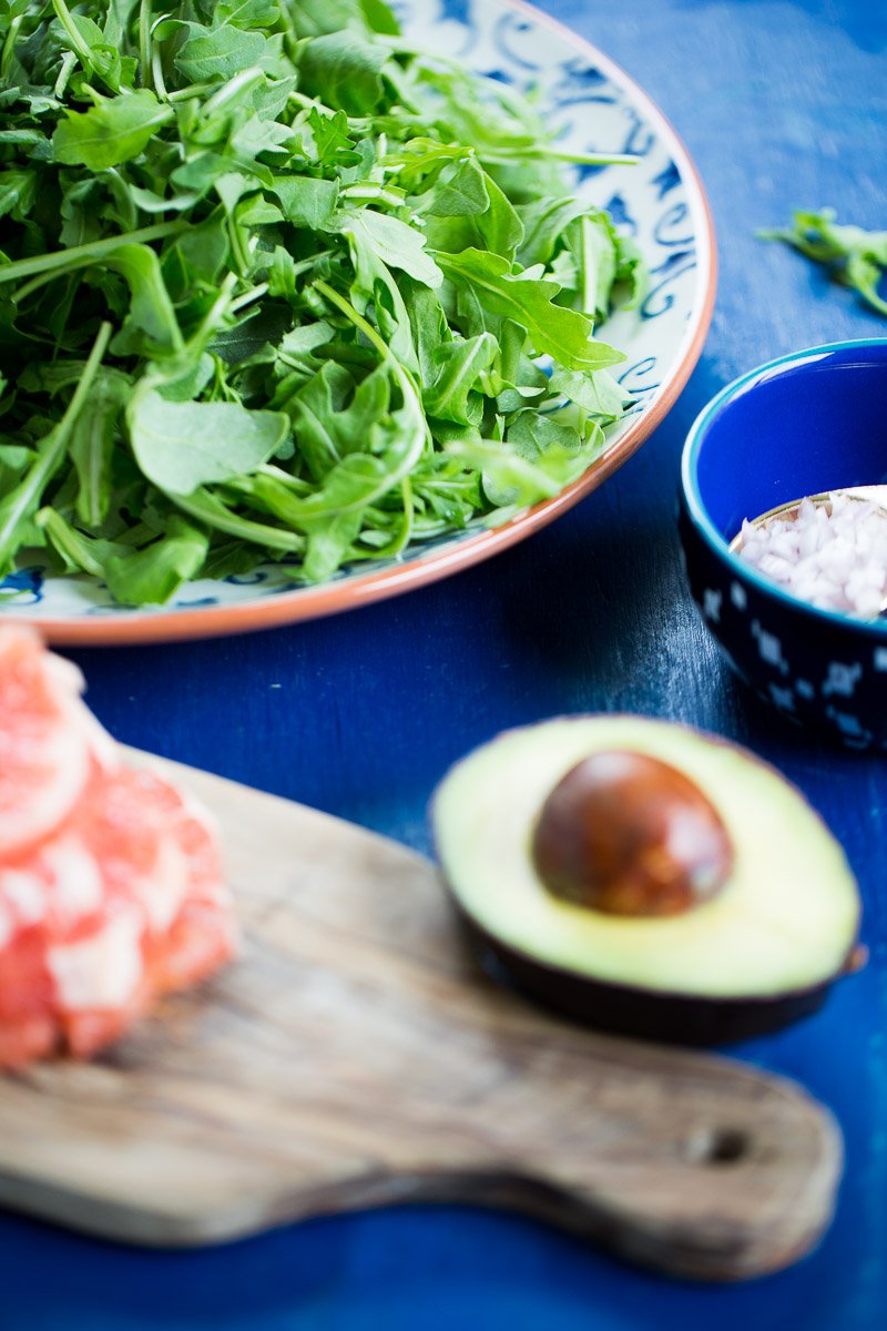A platter with arugula, a halved avocado, diced shallot and grapefruit.