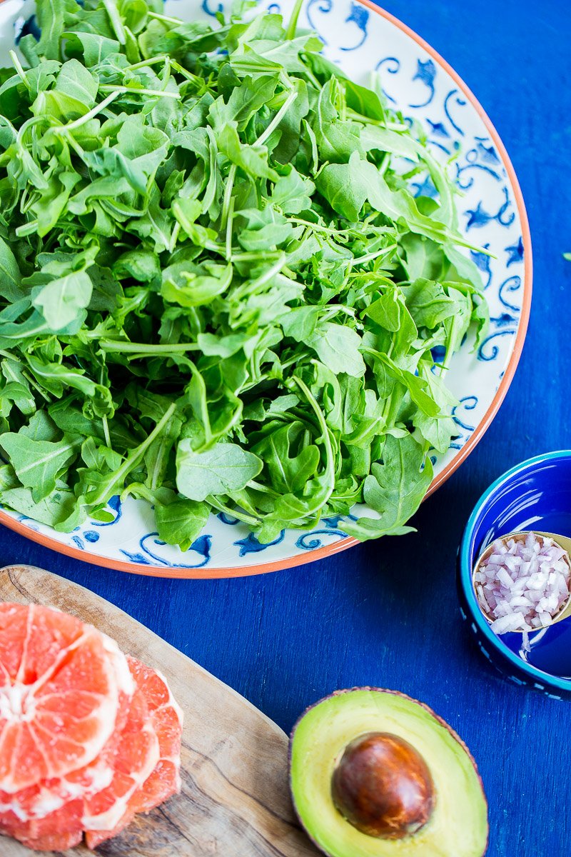 A platter with arugula, a halved avocado, diced shallot and grapefruit.