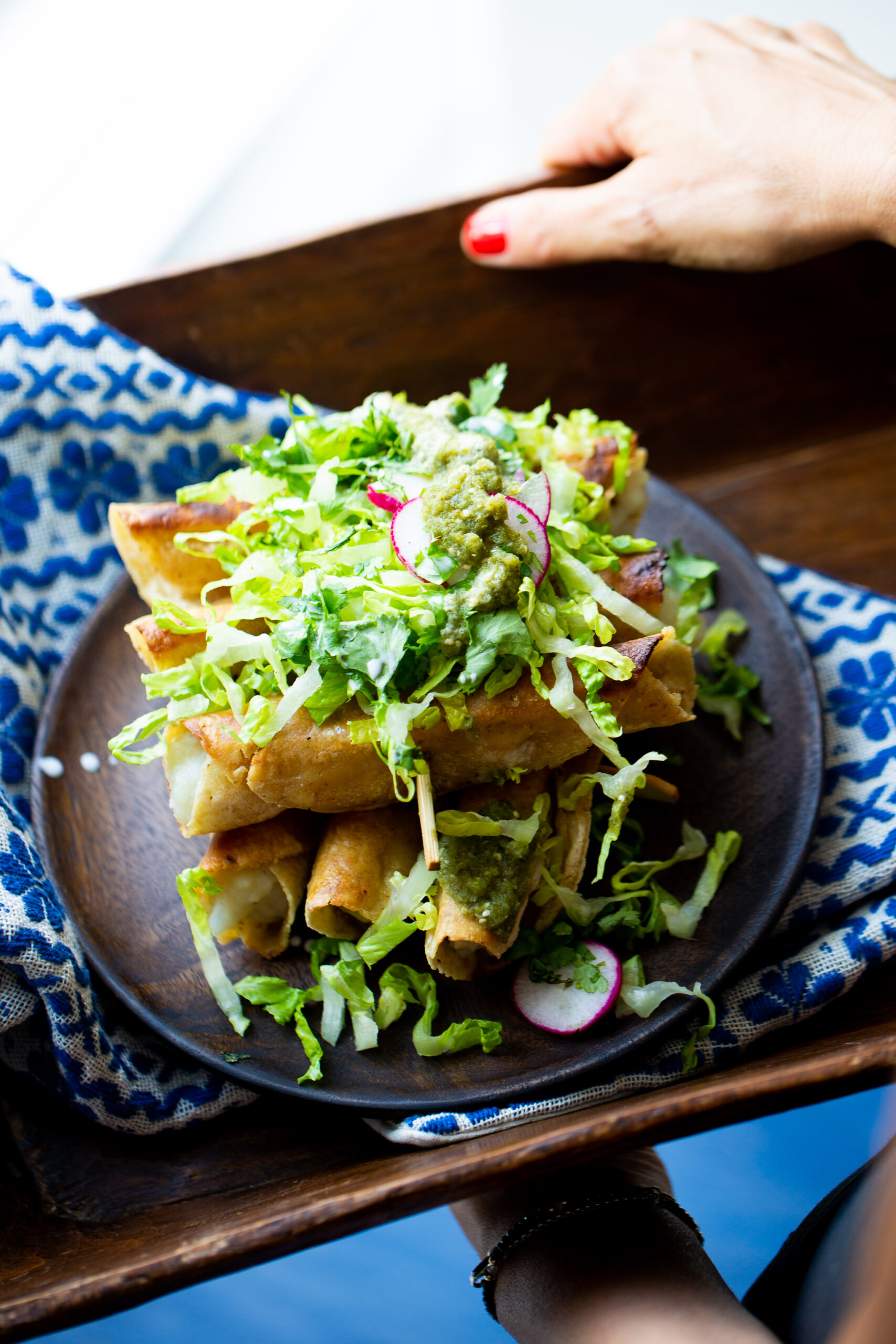 A wooden splate with vegan flautas topped with lettuce and salsa verde.