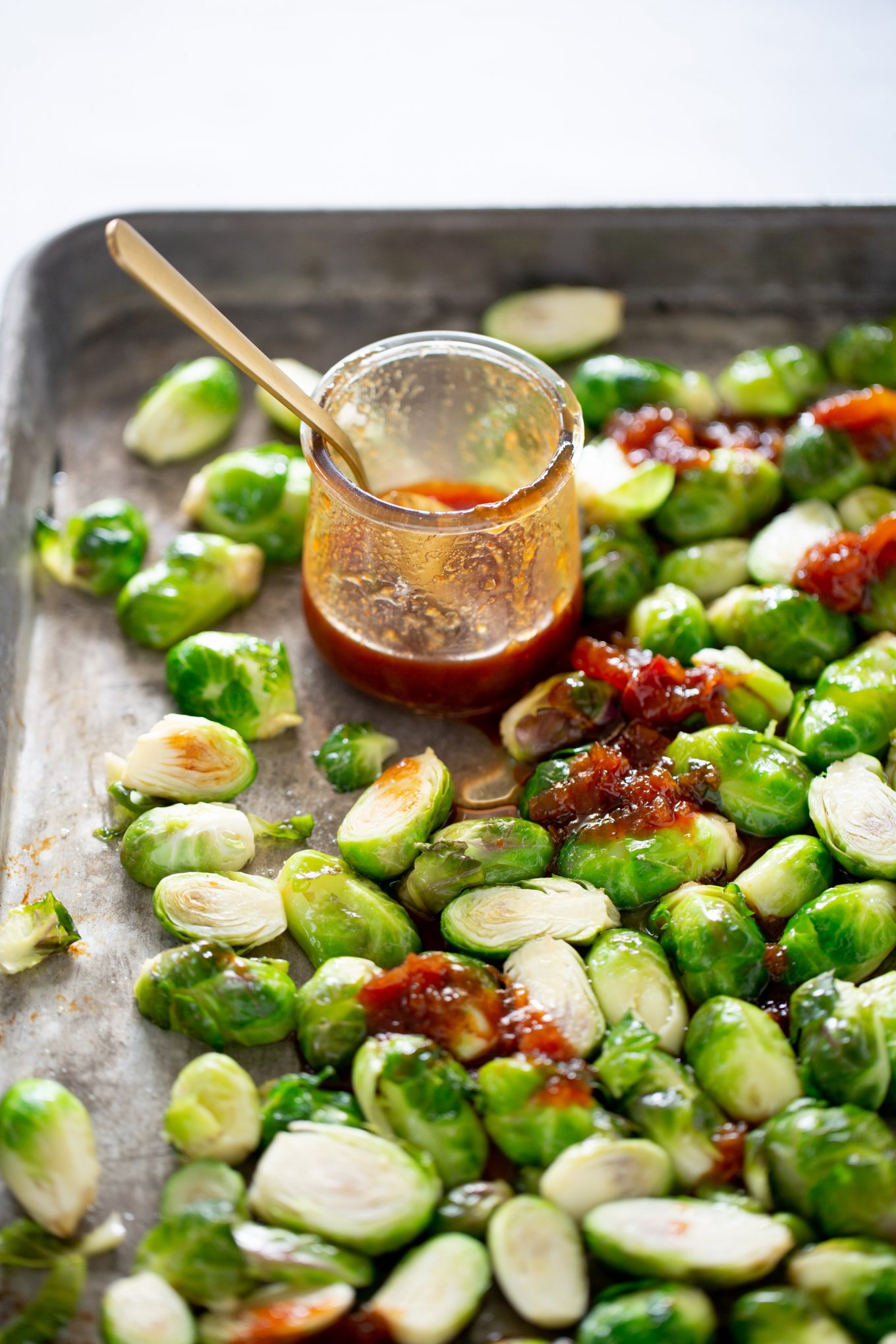 Brussel sprouts on a baking sheet with a jar of sweet ans spicy sauce