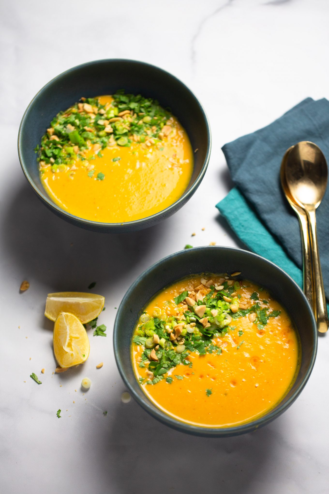 two bowls of roasted kabocha squash soup topped with herbs and peanuts.