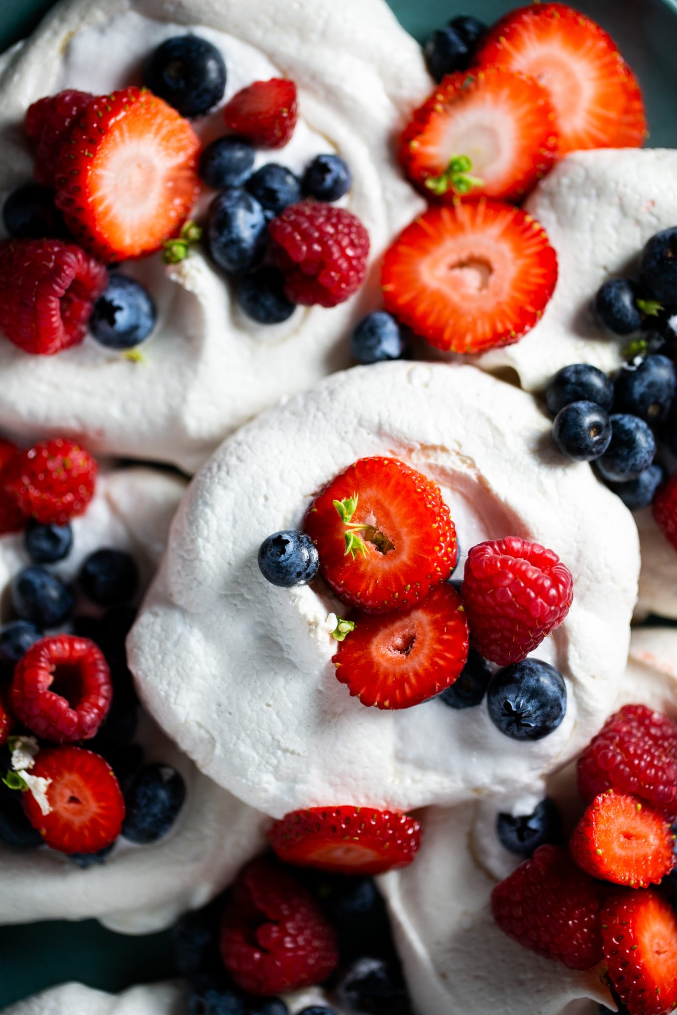 Vegan pavlova topped with sliced strawberries, blueberries and raspberries.