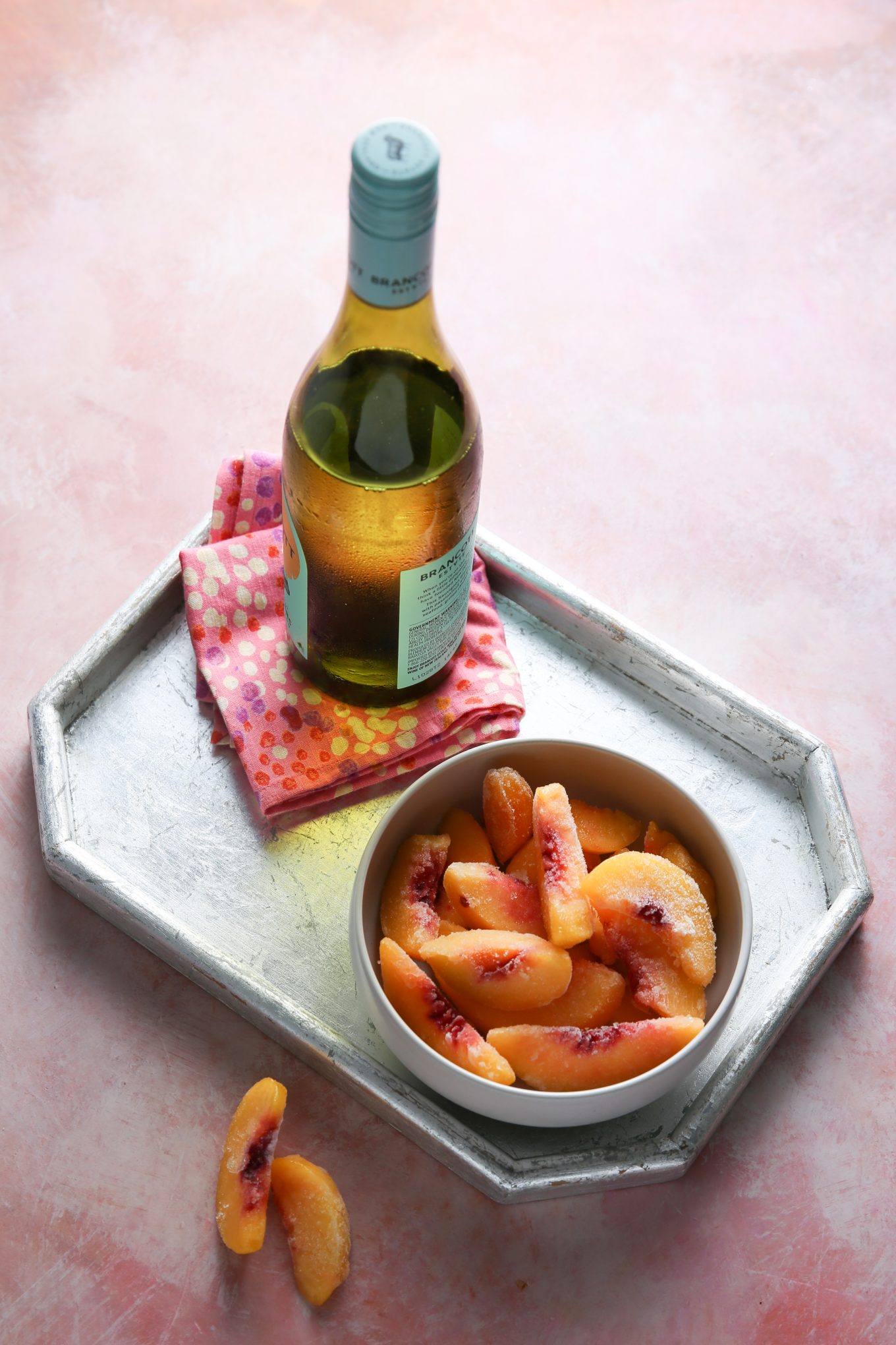 A bottle of white wine and a bowl of frozen peach slices