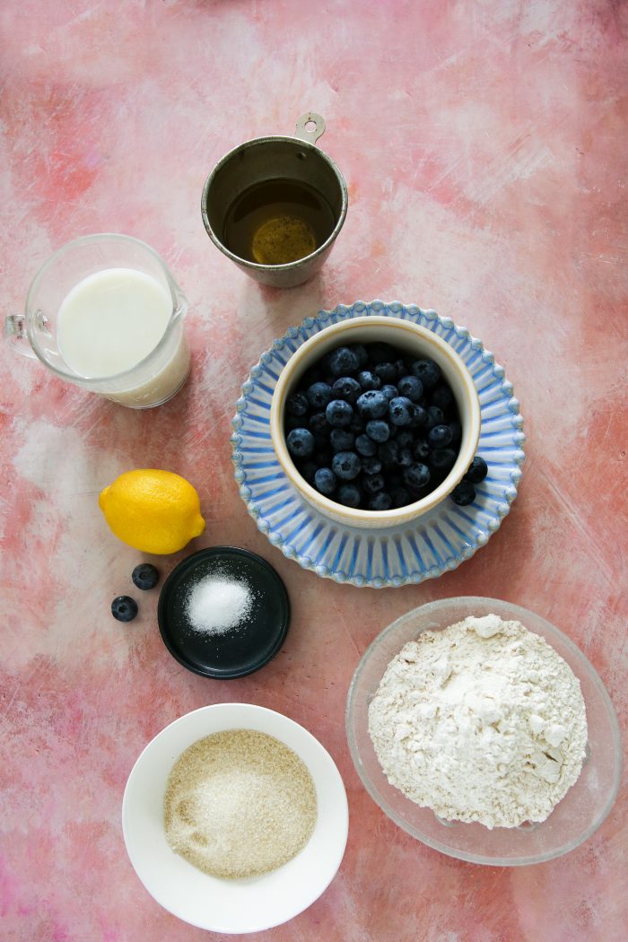 Ingredients in small bowls to make a coffee cake (flour, sugar, salt, oil and milk) and blueberries and a lemon.