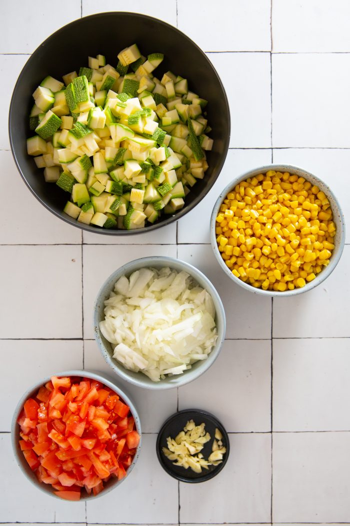 Bowl with diced calabacitas, bowl with corn, another one with tomato, diced onion and garlic.