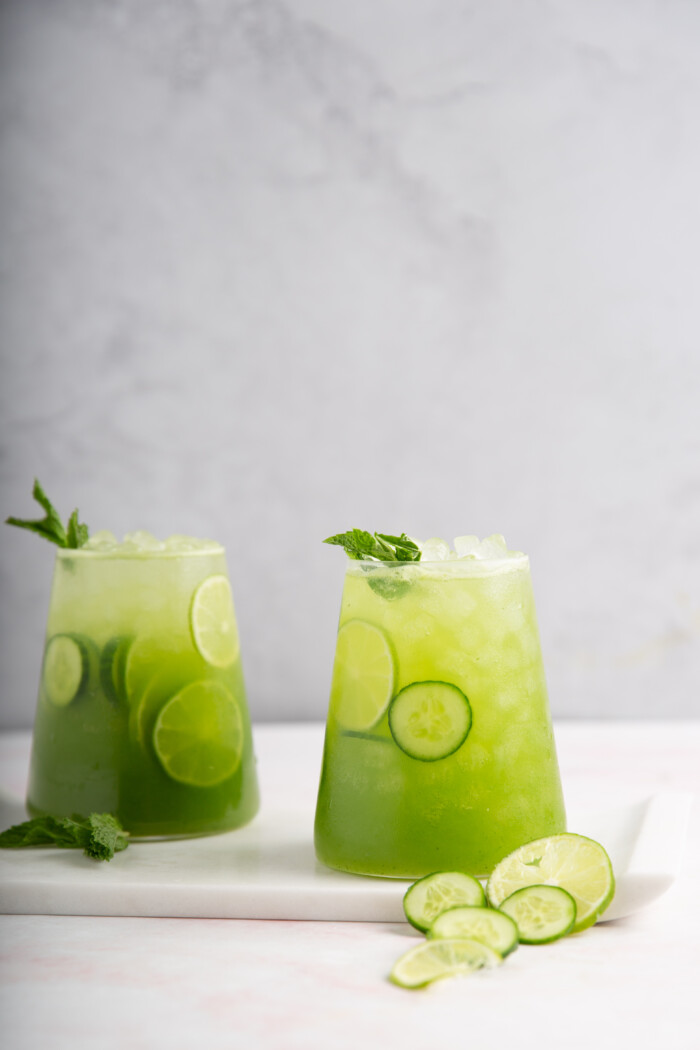 two glasses with cucumber agua fresca with limes and mint