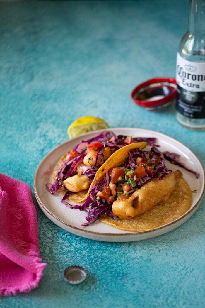 Two corn tortilla vegan fish tacos topped with red cabbage slaw and pico de gallo.