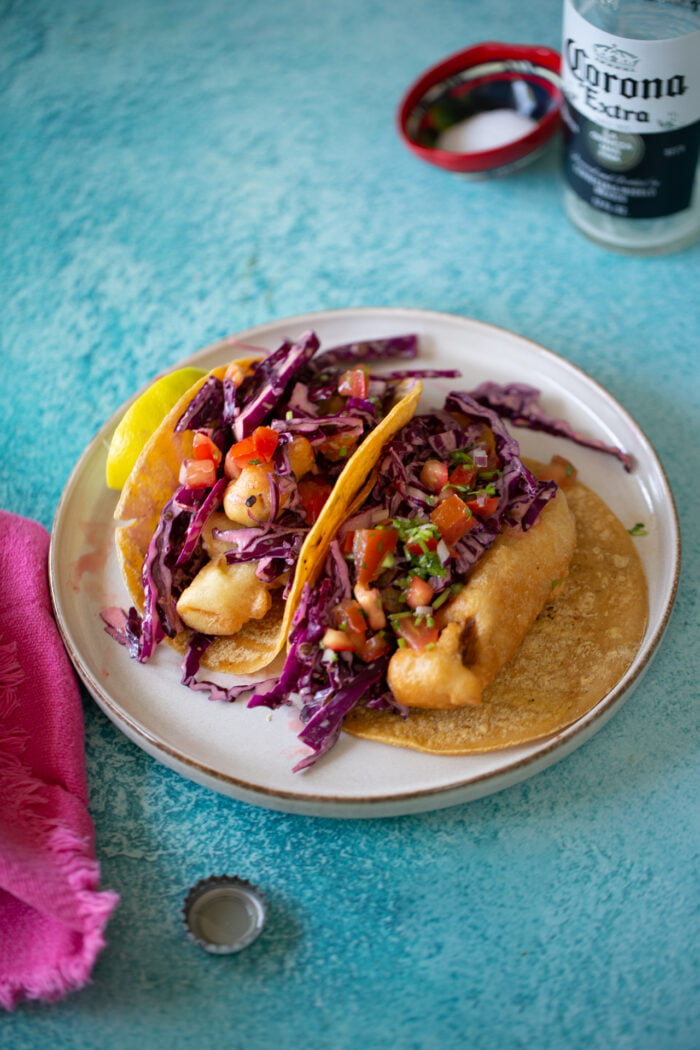 vegan beer battered fish tacos on a neutral plate over a blue table.