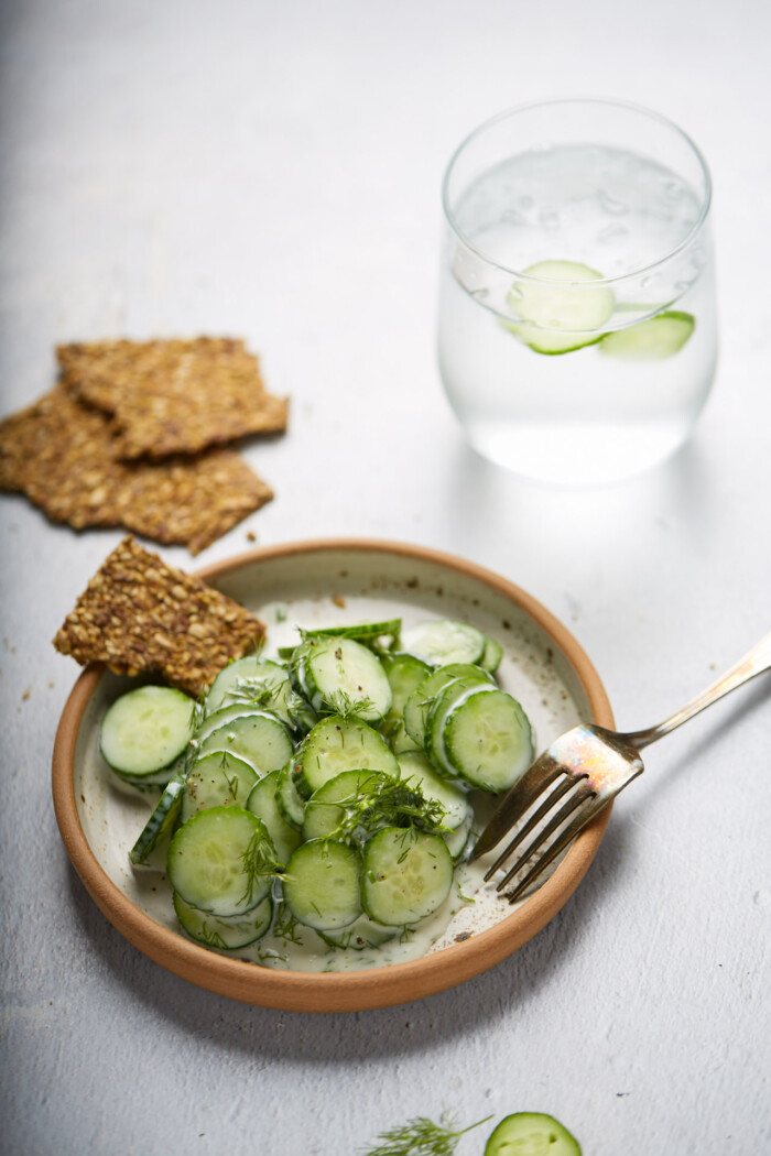 Vegan creamy cucumber dill salad in a small dish with seed crackers and a limade on the side.