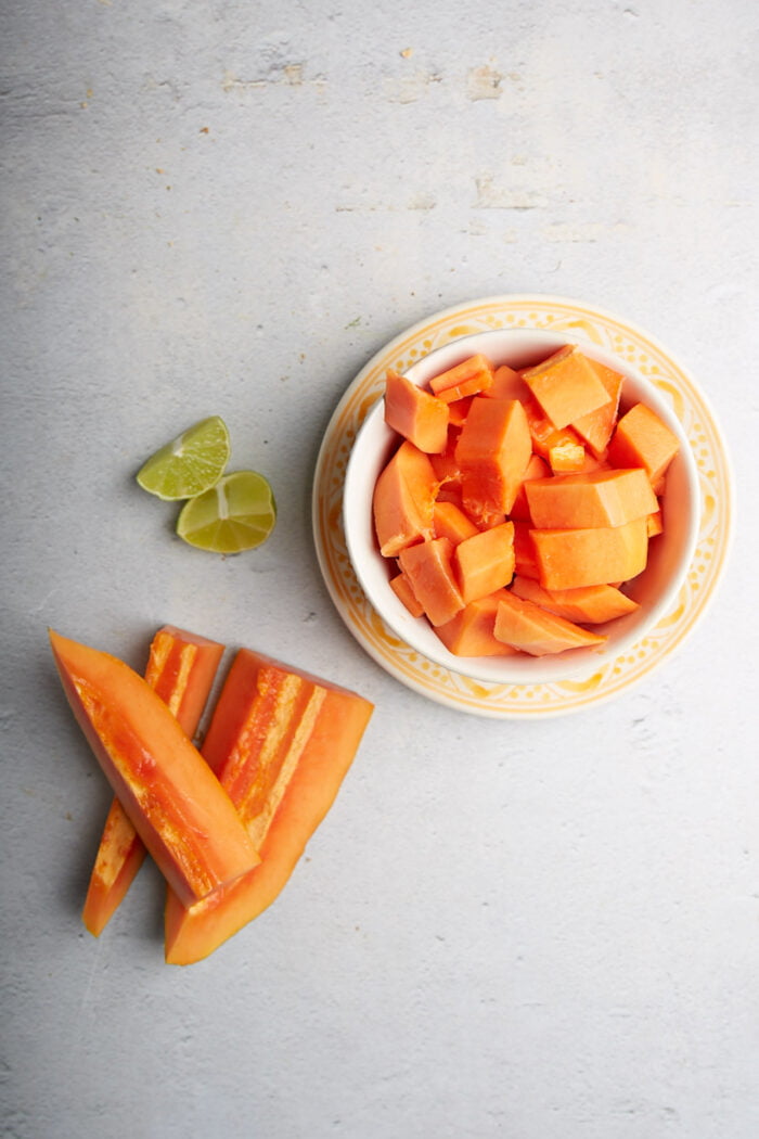 A small plate with papaya chuncks, two slices of papaya and a cut lime.