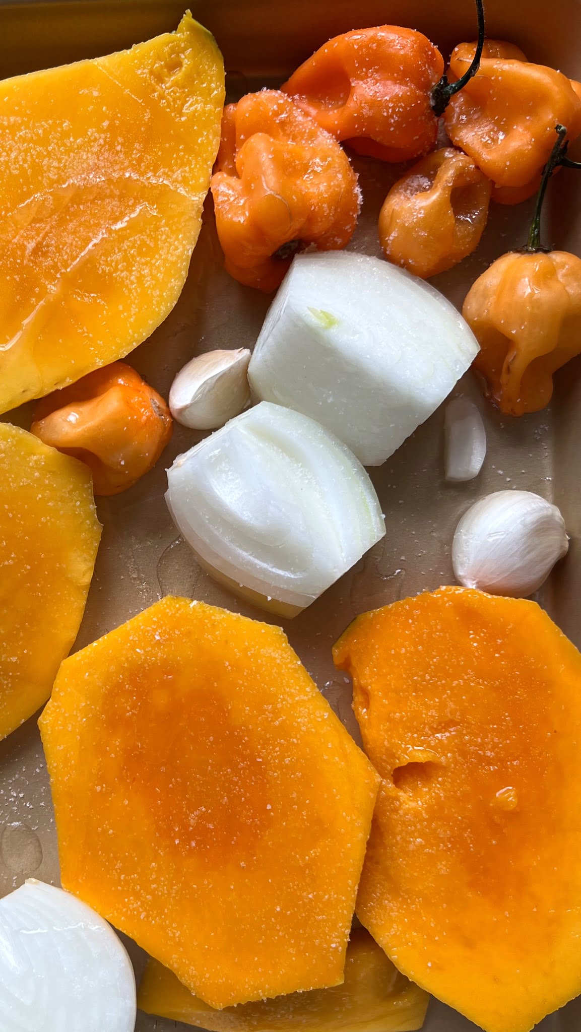 peeled mangoes, quarted white onion and garlic clovees on a baking sheet