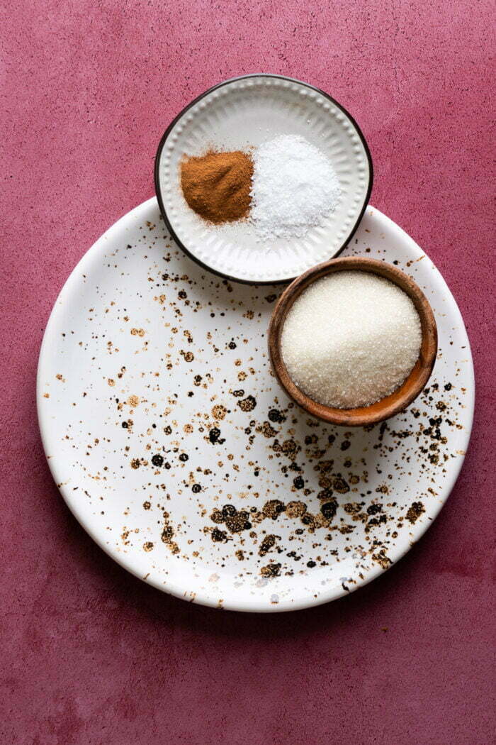 a small white plate with salt and ground cinnamon, a small bowl with sugar over a plate,