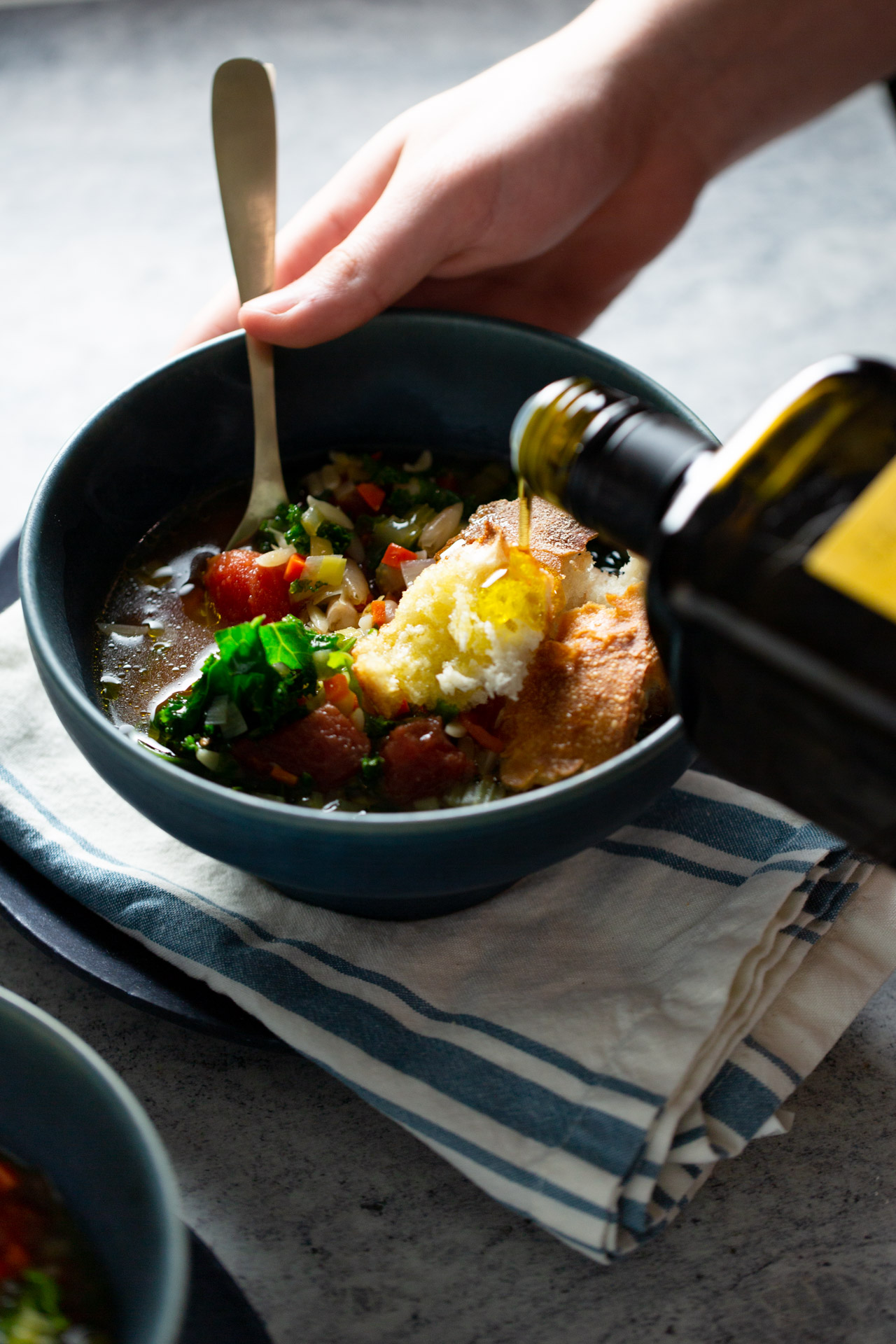 a bowl of soup with bread and olive oil being poured over it.